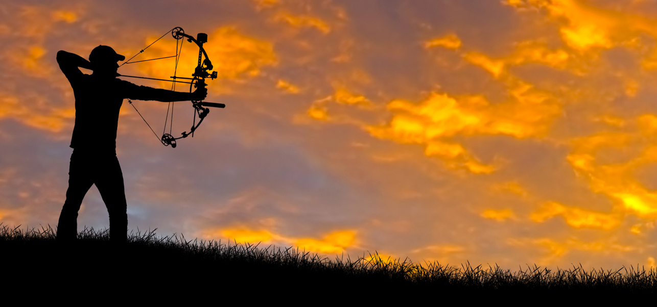 A silhouette of a person preparing to fire a bow, with a bright orange sky in the background.