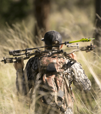 A photo of the back of a hunter dressed in camouflage gear holding a bow.